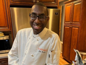 Erik wearing a white chef's coat and standing in a kitchen with a smile.
