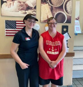 Photo shows Kyle standing next to Emmy, who is dressed for work at Bruegger's Bagels. Both are smiling for the camera.