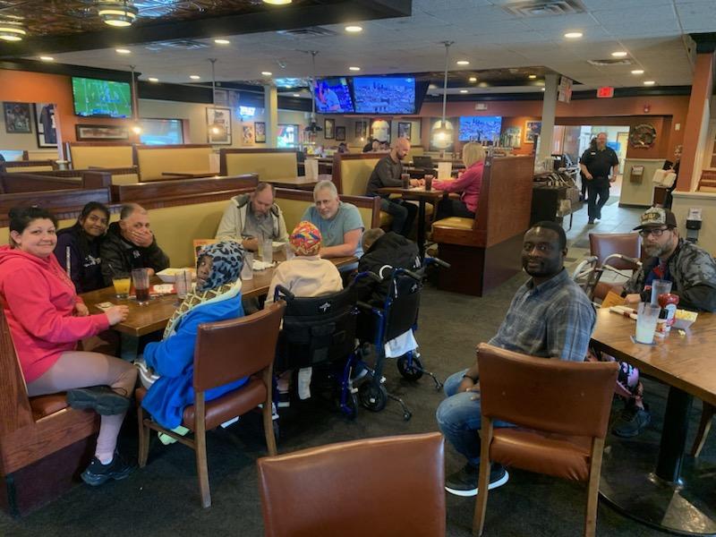 Image shows a group of individuals sitting around a table at a restaurant. Several of them are sitting in wheelchairs