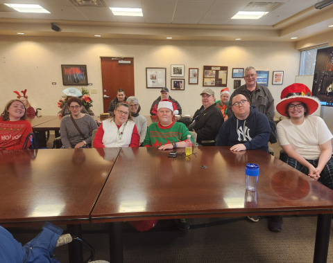 12 people sit around tables. Some are wearing holiday hats or sweaters.