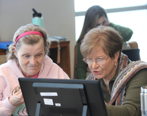 Two women are looking at a computer screen. They seem focused on what they are doing.