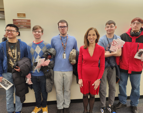 Six people pose for a photo. Students are holding Valentine's Day cards. Assemblywoman Amy Paulin stands in the middle. Her name can been seen on a sign outside her office.