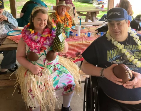 Individuals dressed in grass shirts and leis sit around a picnic table