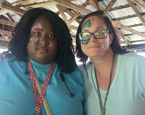 Two individuals look towards the camera. They each have their faces painted to look like butterflies.