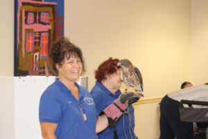 A bird handler holds a hawk in one gloved hand and smiles at the camera