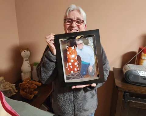 A woman is holding up a framed photo of herself. She is smiling.