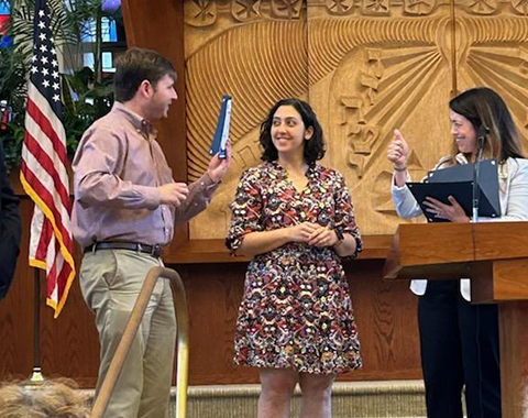 A man holds up his certificate on a stage to two women.