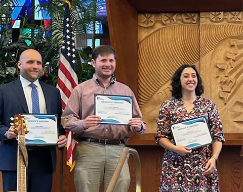 Two men and a woman stand on a stage holding certificates