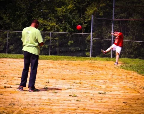 A person kicks a kickball during a game.
