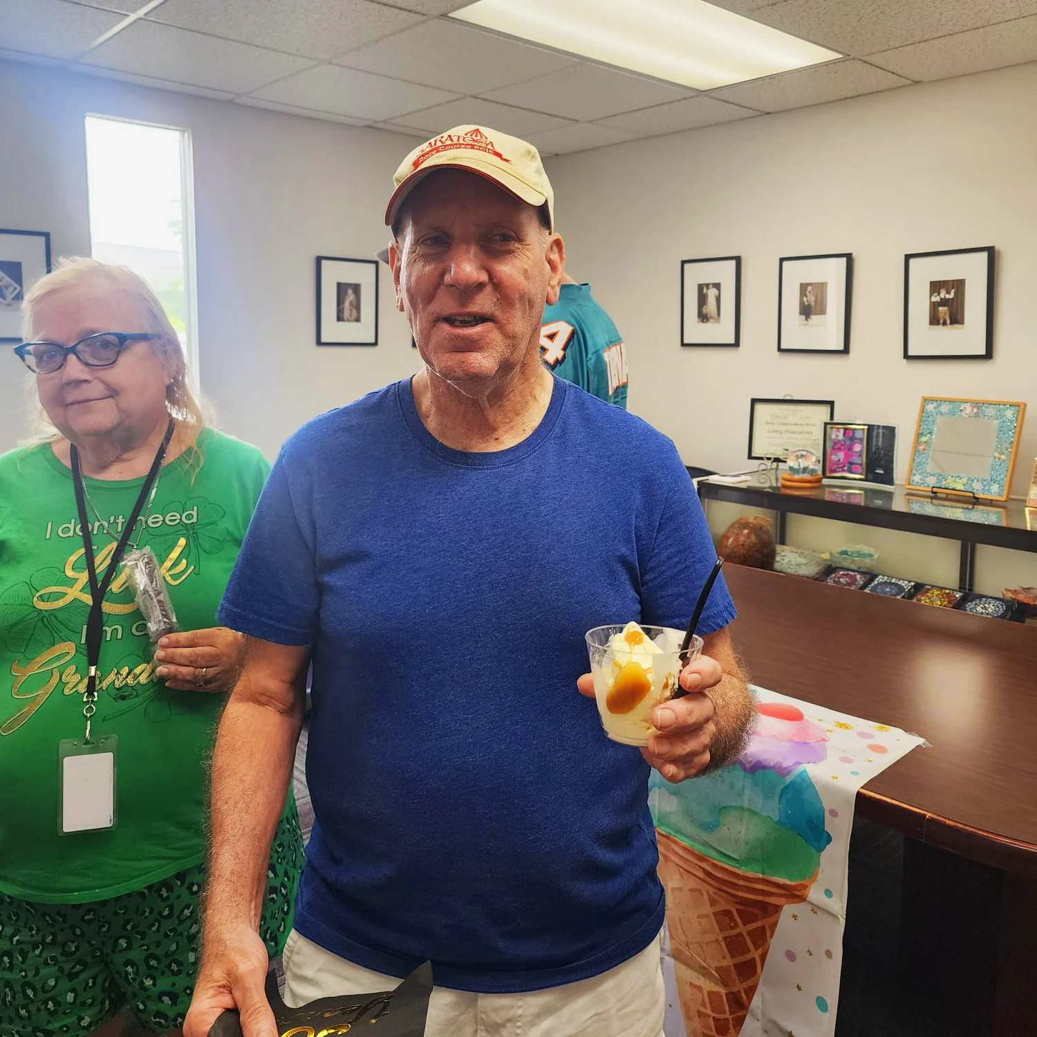 Ice cream social 3 A man in a blue shirt and tan hat holds a cup of ice cream in a clear container in his hand.