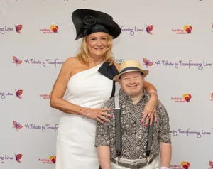 A man and a woman stand and pose for the camera. The woman has her arm around the man.