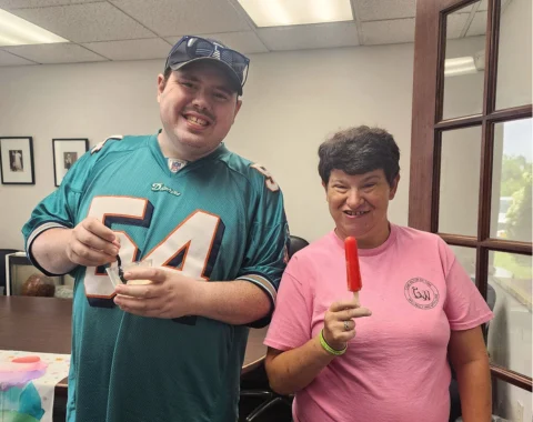 A man and a woman smile for the camera. The man holds a cup of ice cream and the woman holds a red popscicle