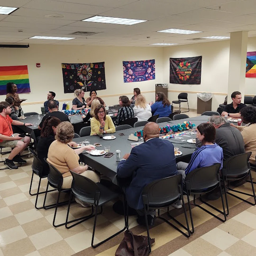 A room of people gather at tables at a party to eat food and talk.