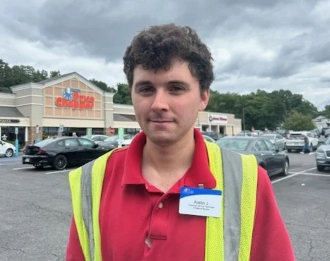 Image of a man in his grocery store uniform standing outside the market where he works.