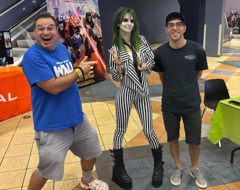 Two men stand with a woman in a beetlejuice costume.
