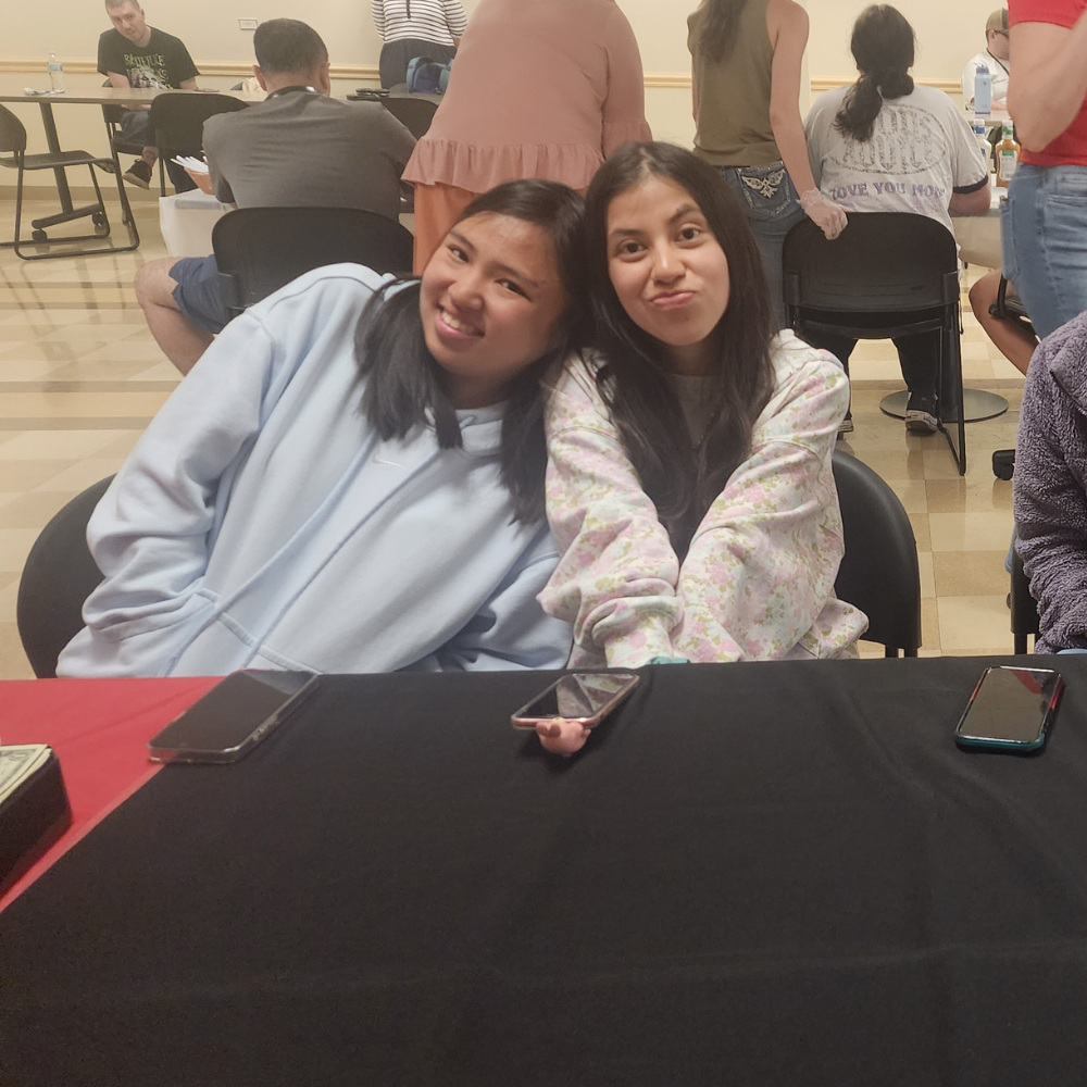 3 Two female college experience students pose for a photo at a table with a black tablecloth on it.