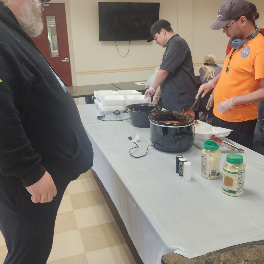 4 students serve spaghetti to a patron of their fundraiser.