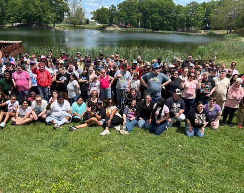 A large group of people in Living Resources' Day Community Opportunities Program pose for a photo near a pond.
