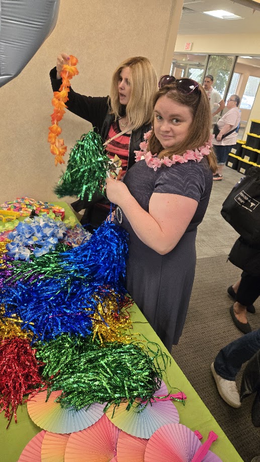 20260721_130338 Two women select from a table of fun lei's and decorations for the disability pride parade at living resources.