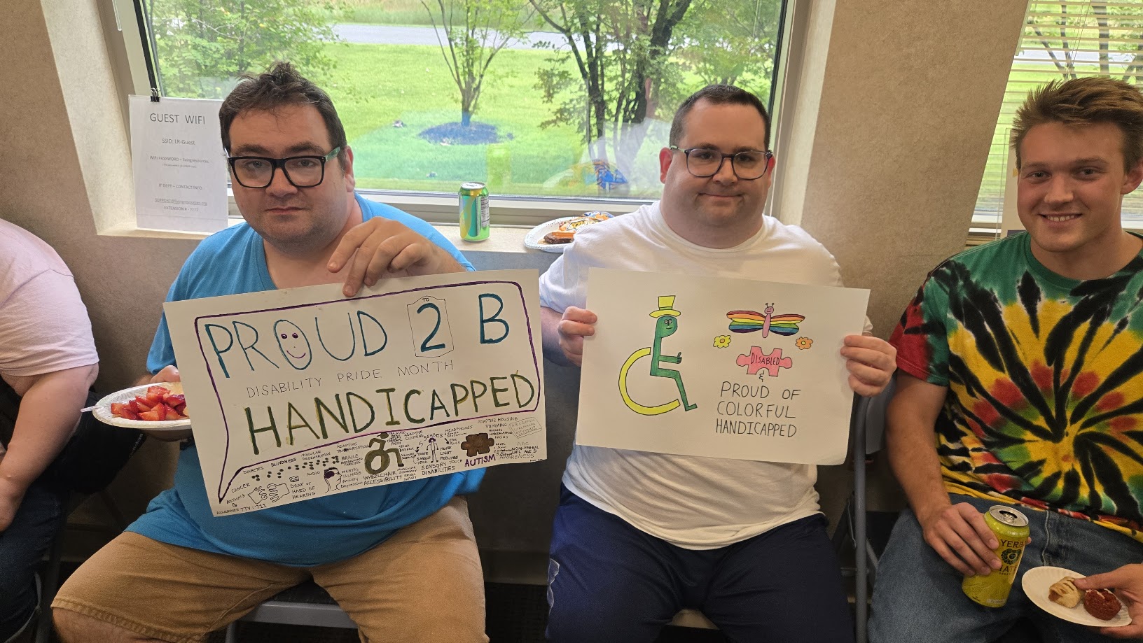 20260721_131618 Three men sit in a row. the two men on the left are holding up disability pride month signs they made in art class. One sign reads "Proud 2 b Handicapped" and the other reads "proud of colorful handicapped"