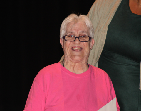 Day Services Awards 1 A woman with short white hair and glasses smiles for the camera. She is wearing a pink t-shirt.