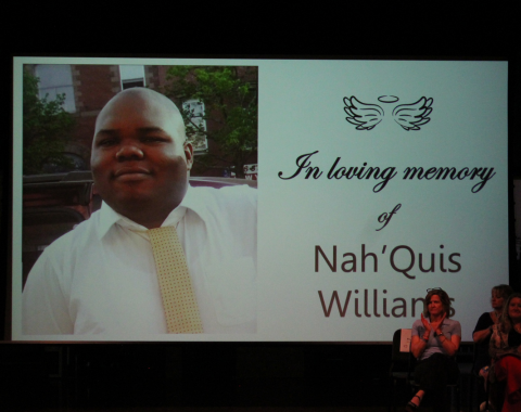 Day Services Awards 5 A photo of a man wearing a while button up shirt is on the screen of an auditorium. Next to his photo it reads In loving memory of Nah'Quis Williams.