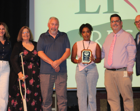 Day Services Awards 7 6 people stand on a stage. The woman in the center is holding the Amanda R. Rivenburg Phoenix Award at the living resources day services awards.